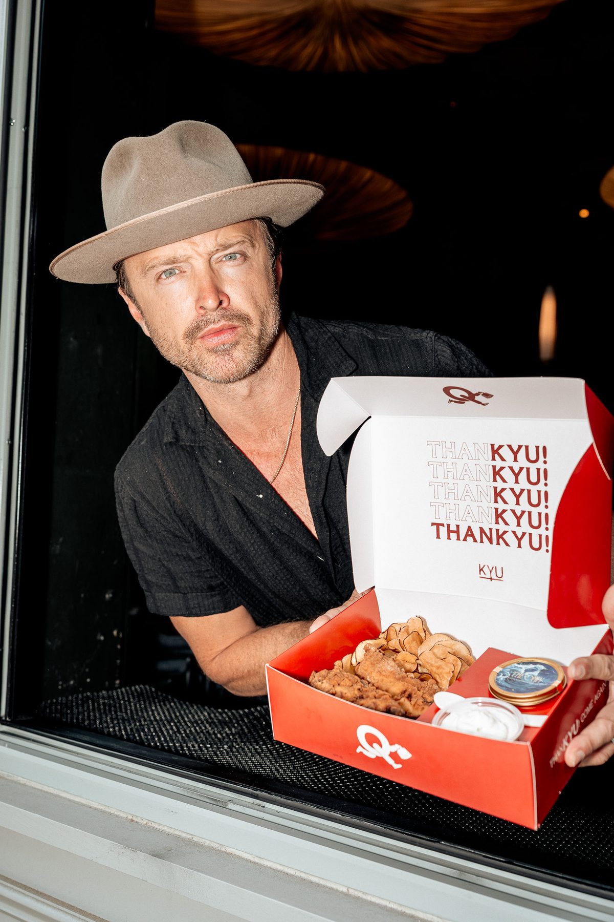 Aaron Paul handing a ThanKYU box out through the takeout window