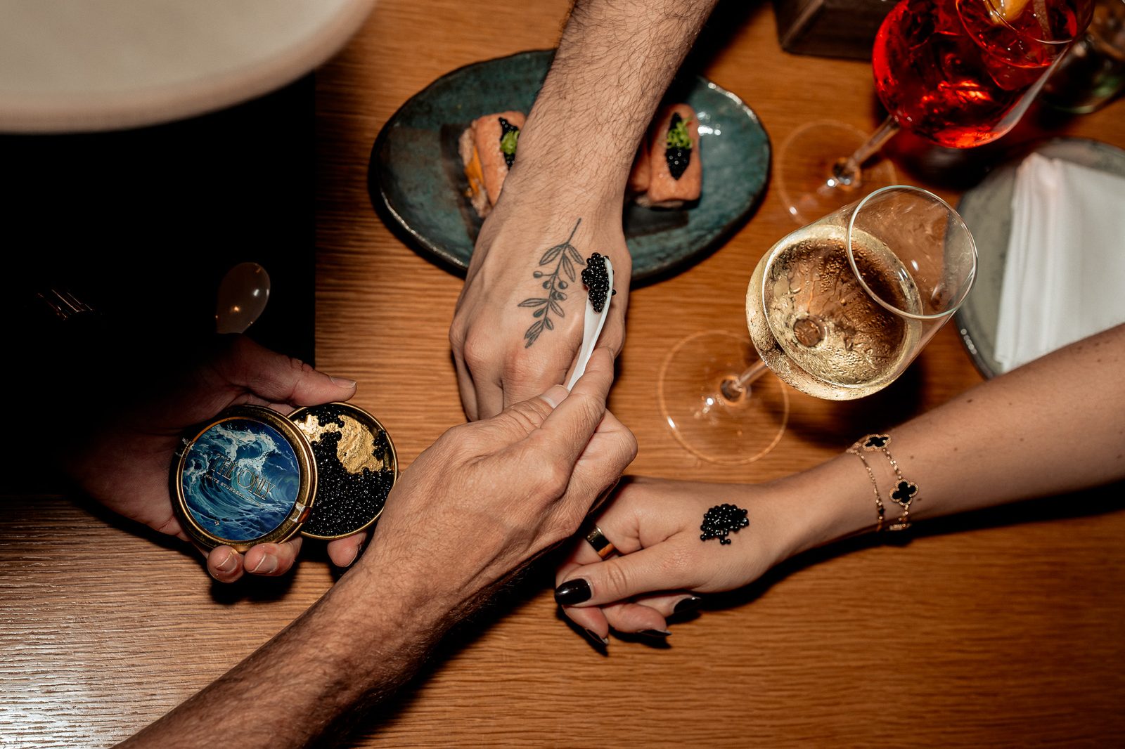 Overhead of hands at the table taking caviar bumps beside drinks and plates