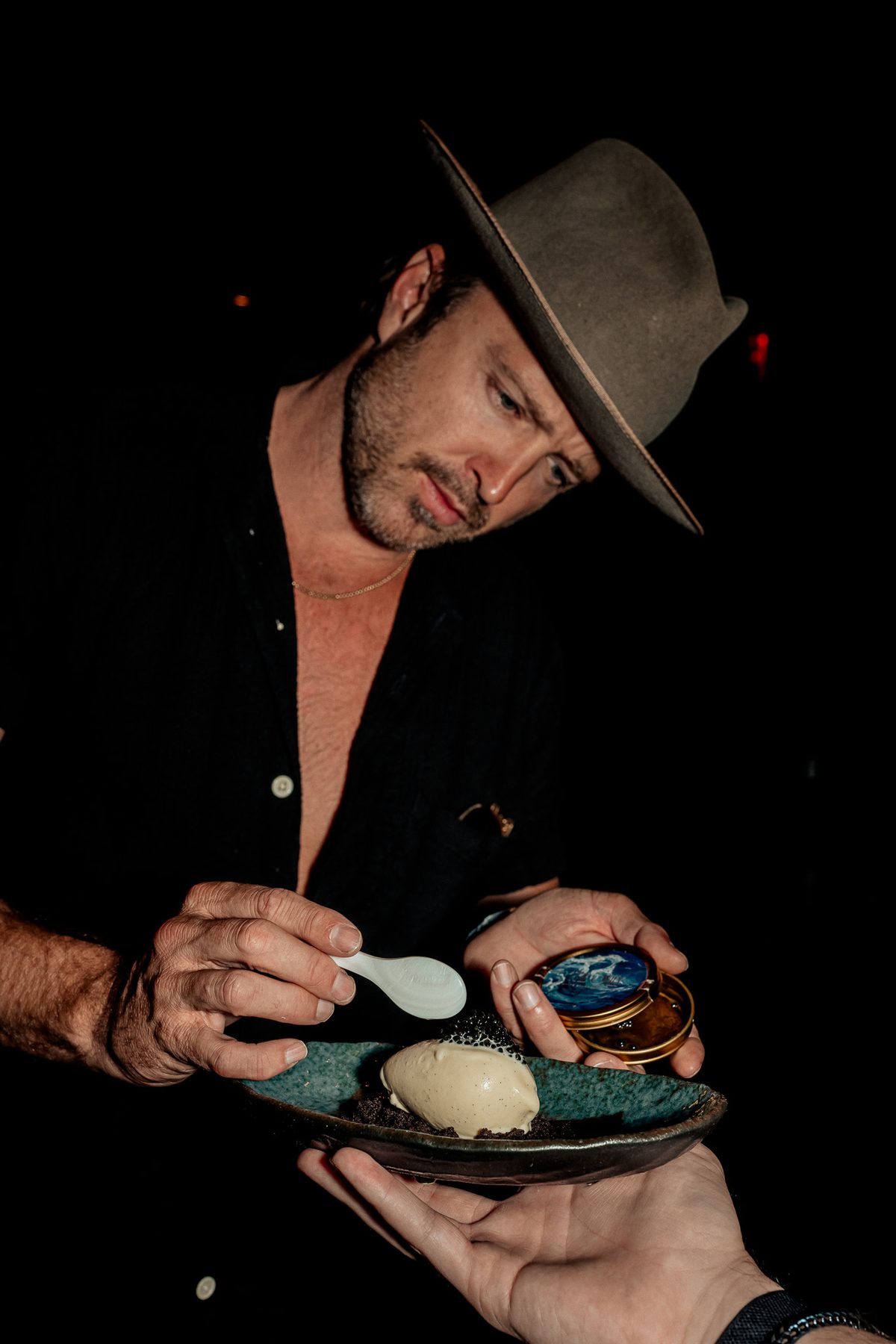 Aaron Paul spooning caviar from the tin onto a scoop on a dark plate