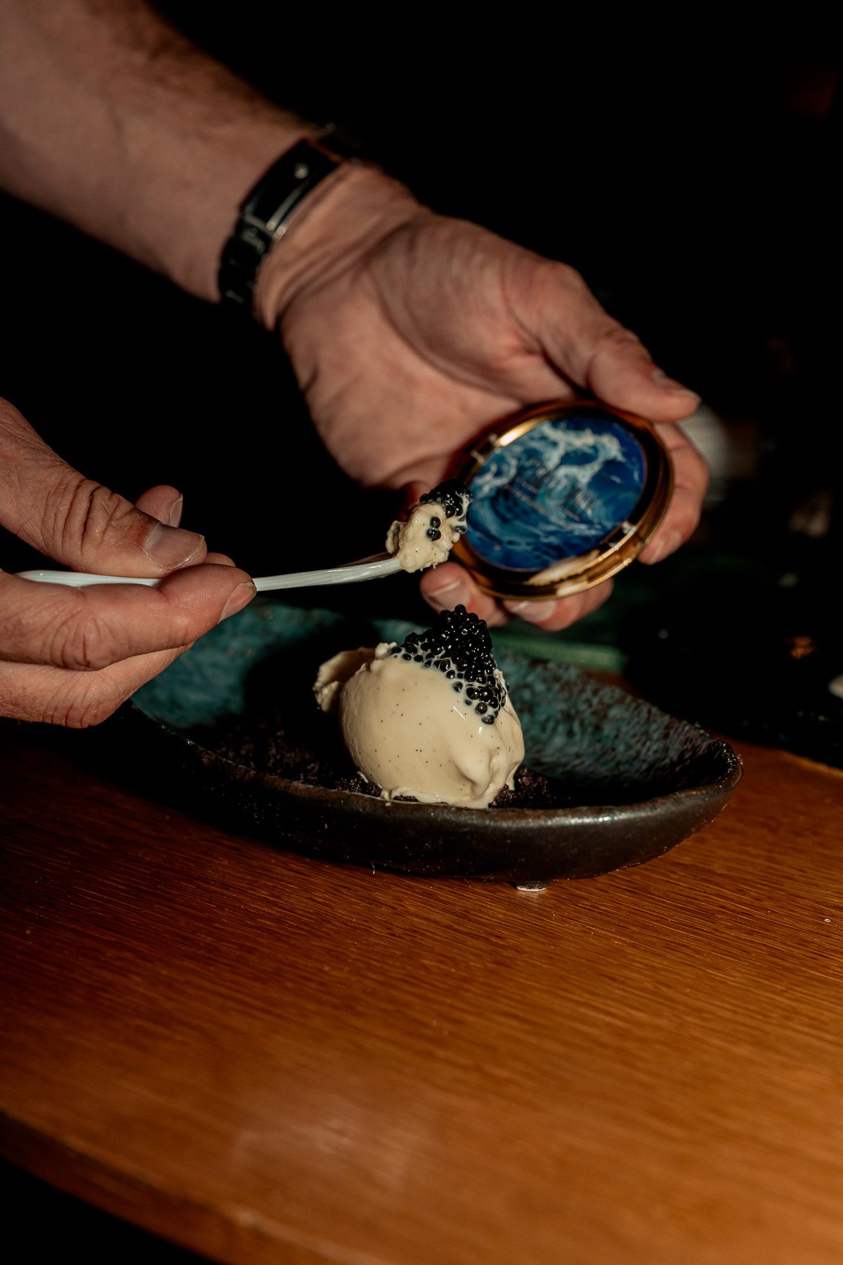 A spoon of caviar going onto a scoop on a dark plate at the bar